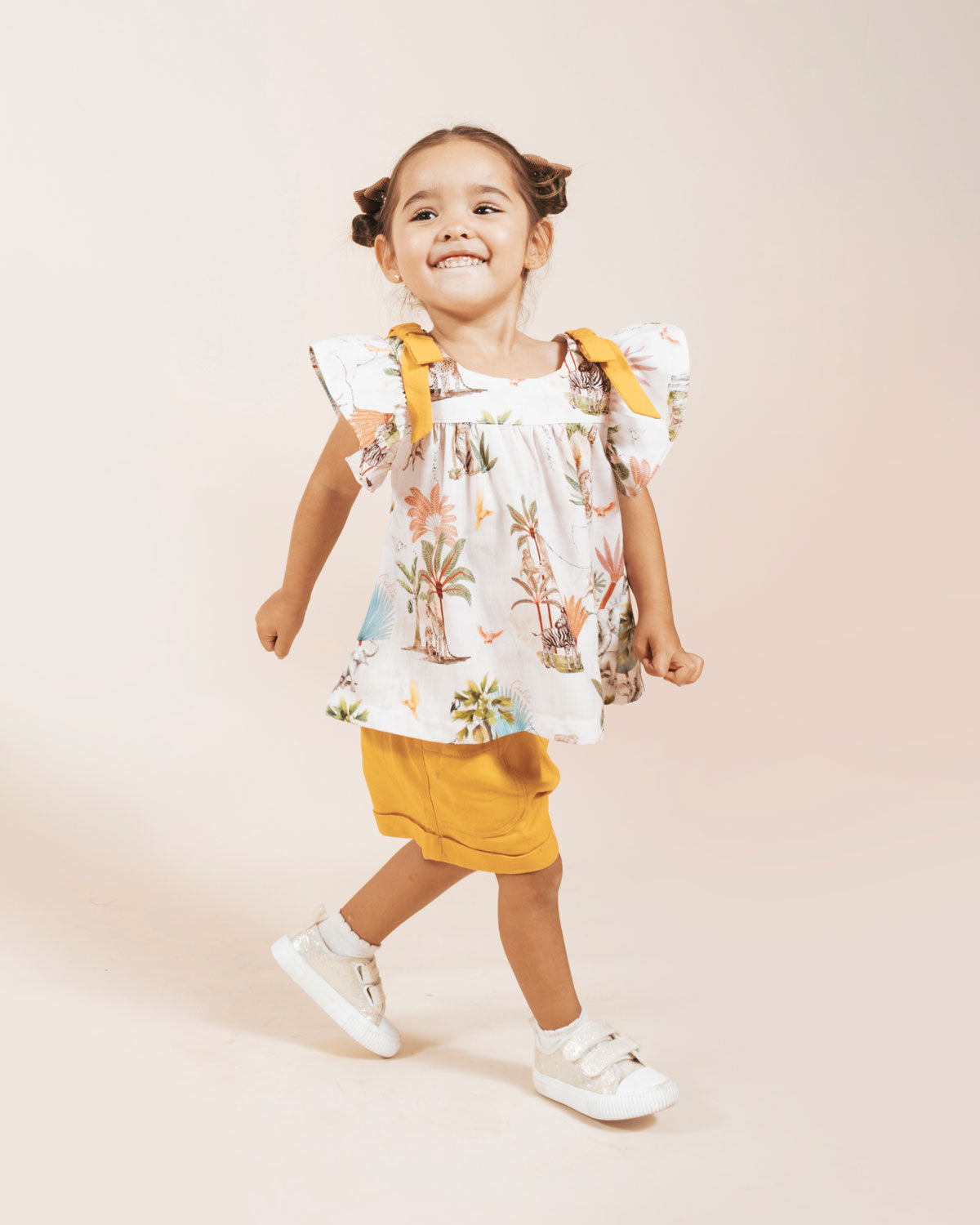 Conjunto blusa estampada con detalle de moños en hombros y short mostaza para niña