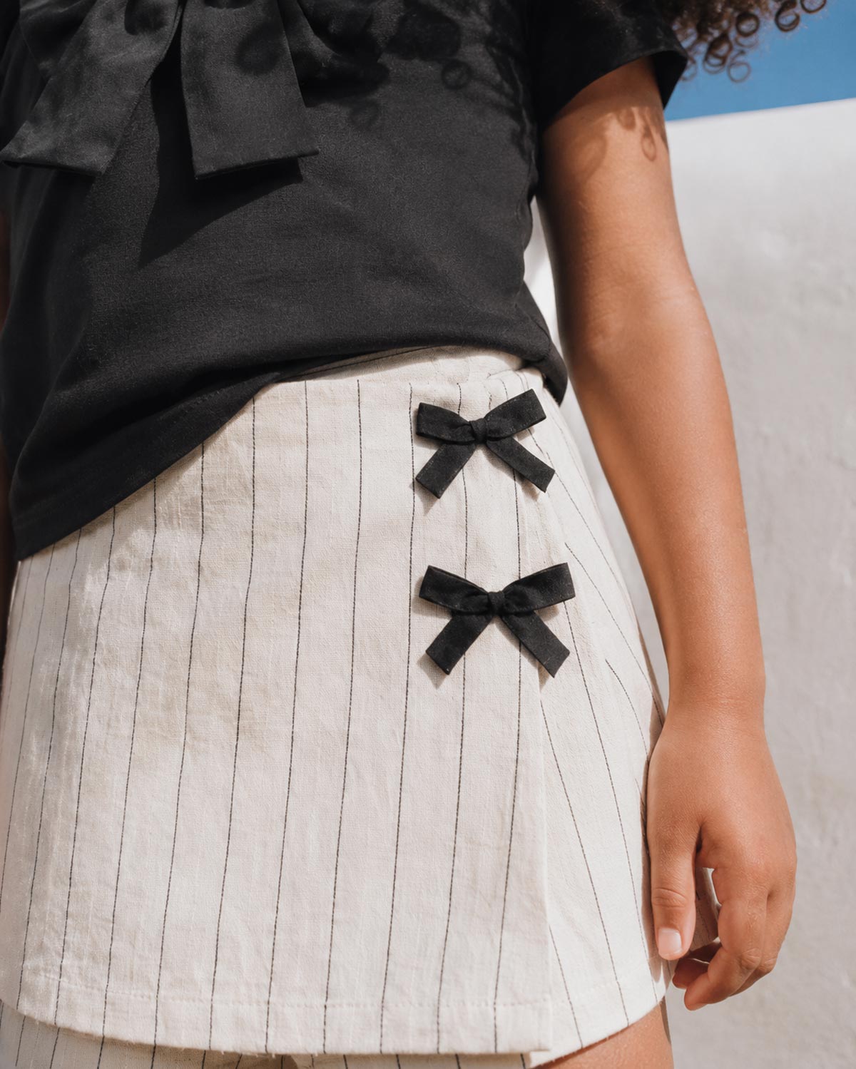 Conjunto blusa negra con moño y falda short en lino con rayas y moñitos para niña