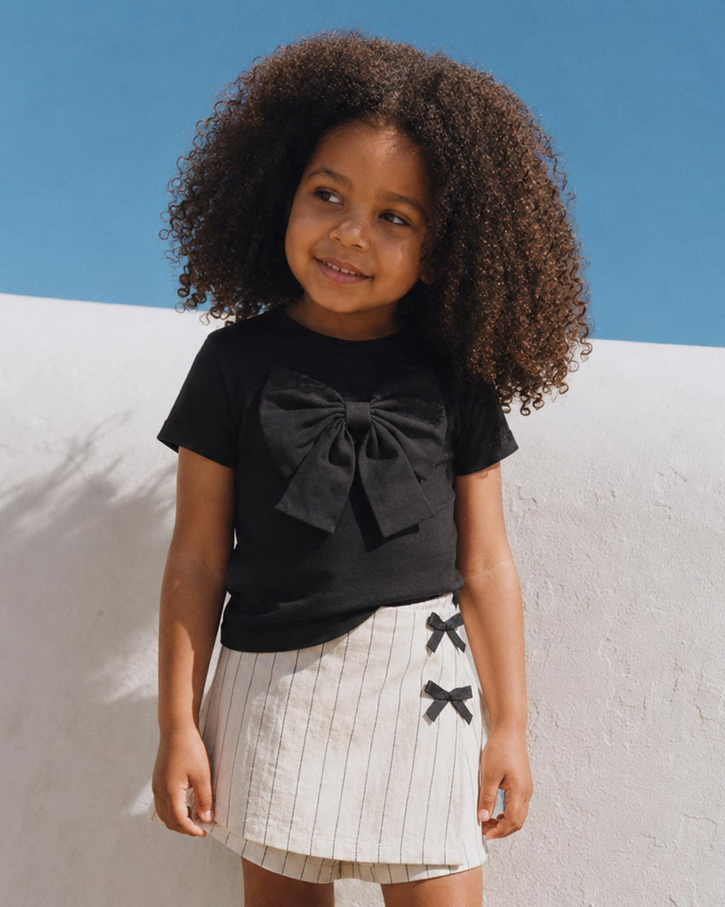 Conjunto blusa negra con moño y falda short en lino con rayas y moñitos para niña