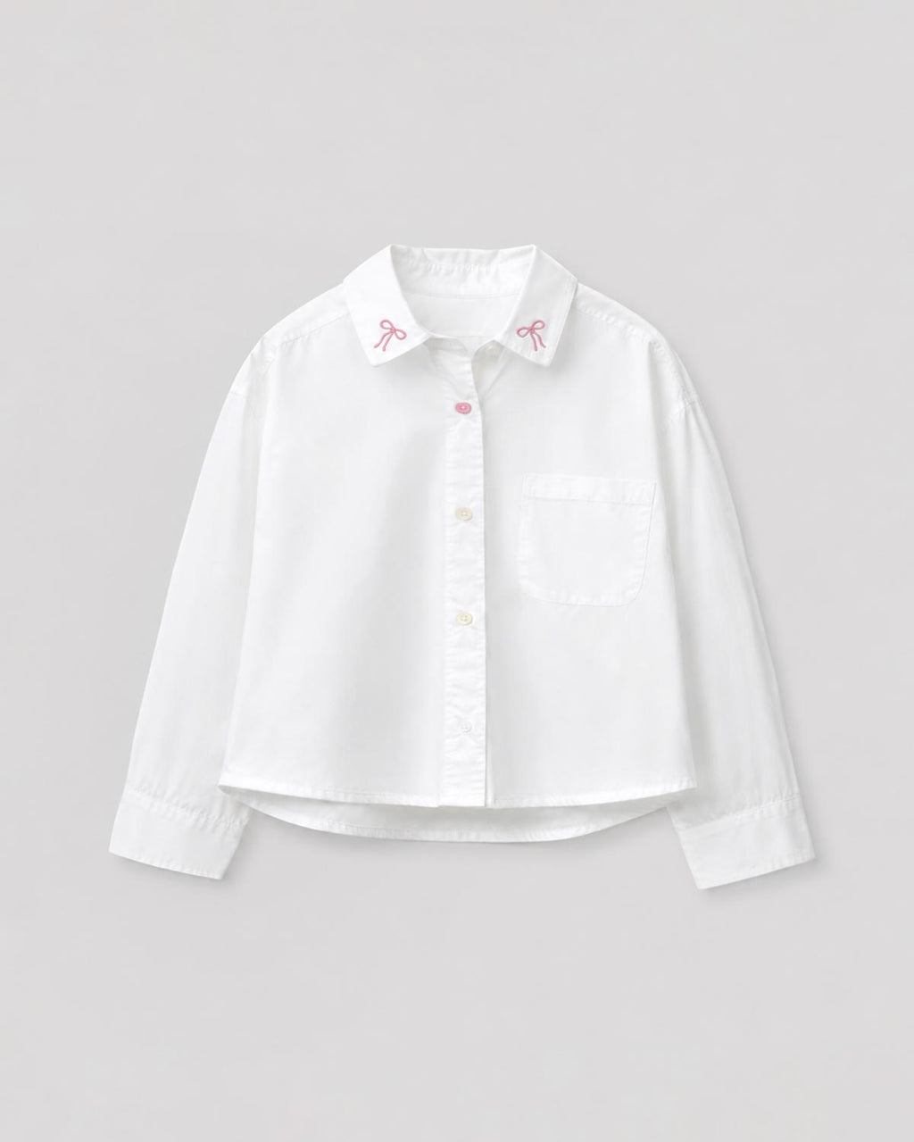Camisa blanca con pequeño bordado de moños y bolsillo para niña